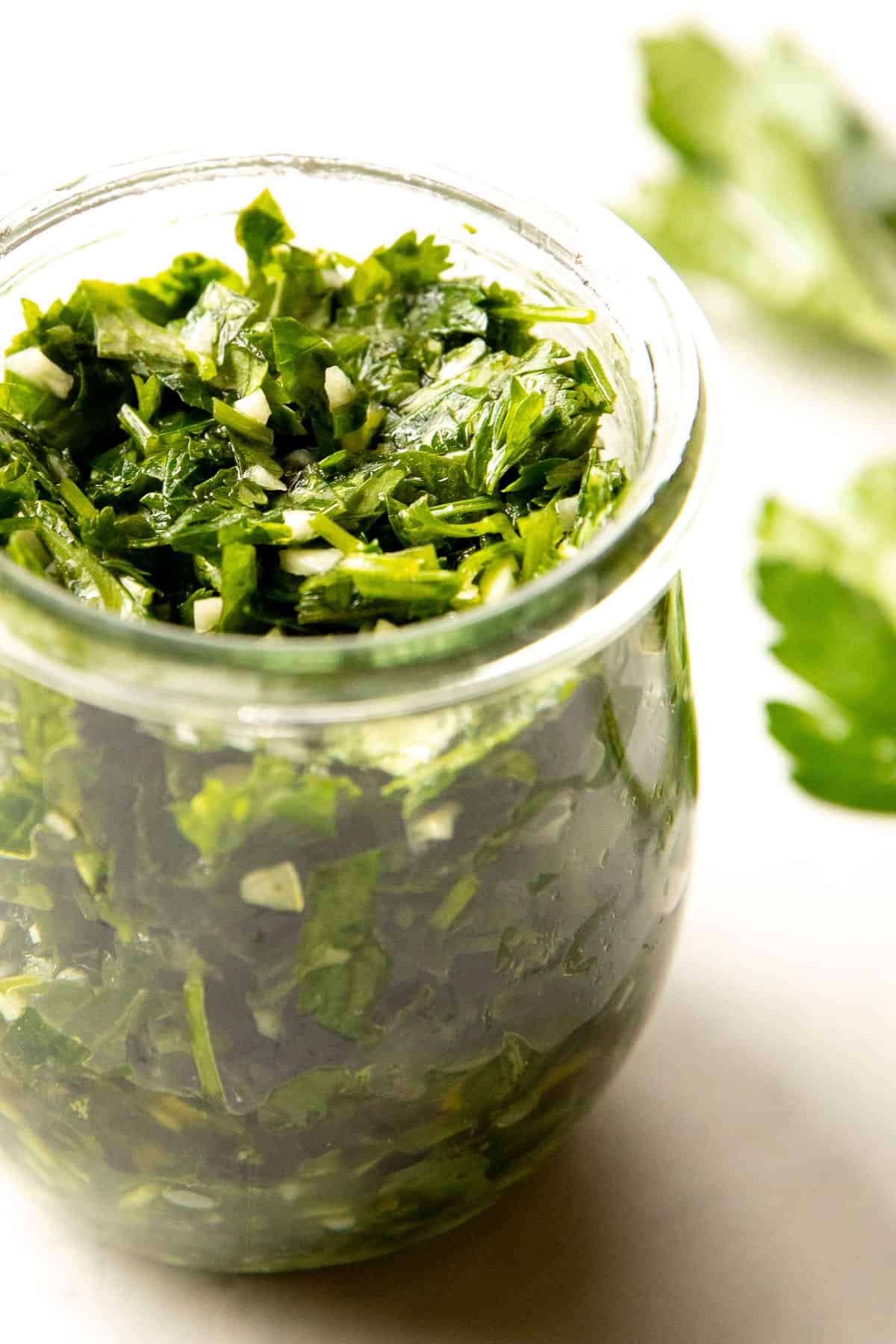 chimichurri sauce in a jar with parsley in the background