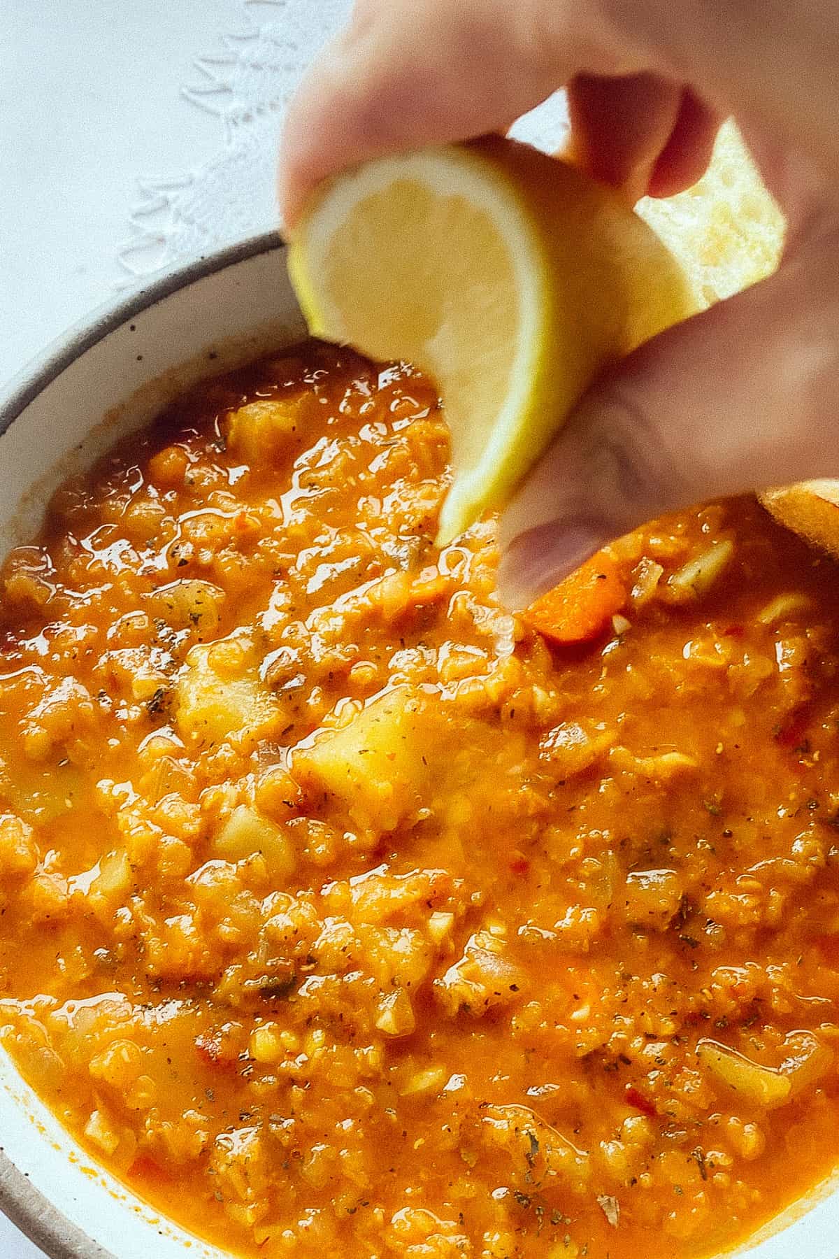 hand squeezing lemon onto red lentil soup